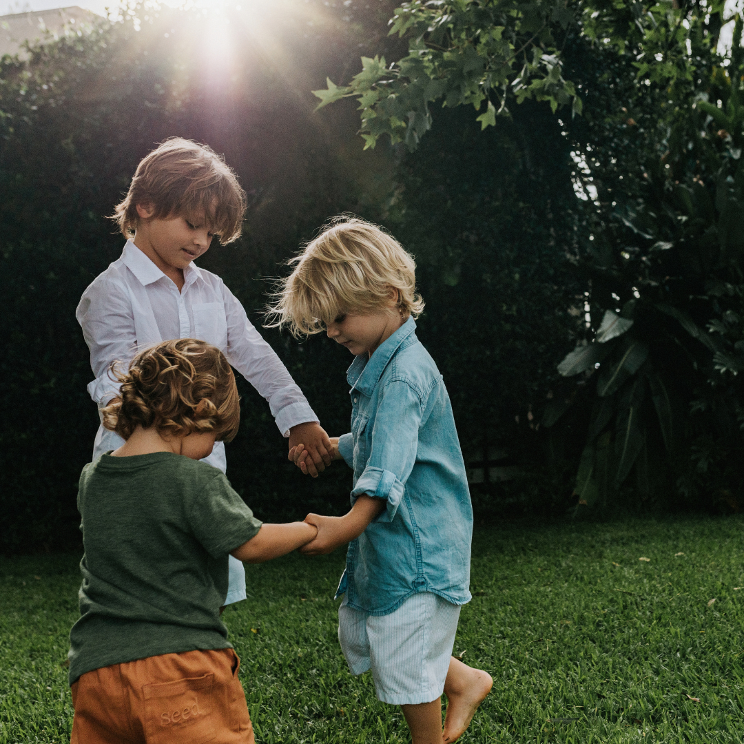 Three boys holding hands in a circle outdoors on the grass
