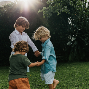 Three boys holding hands in a circle outdoors on the grass